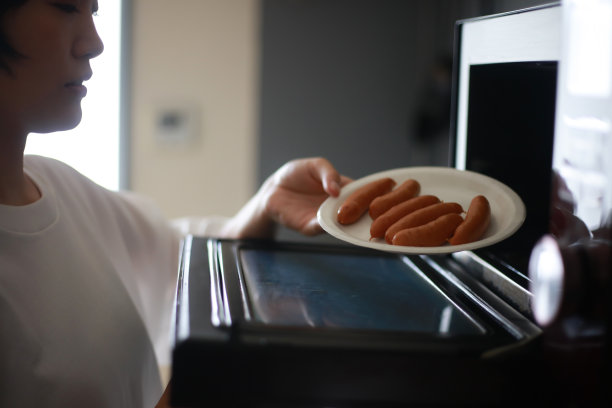 一个女人把香肠放在纸盘上，然后用微波炉加热图片下载