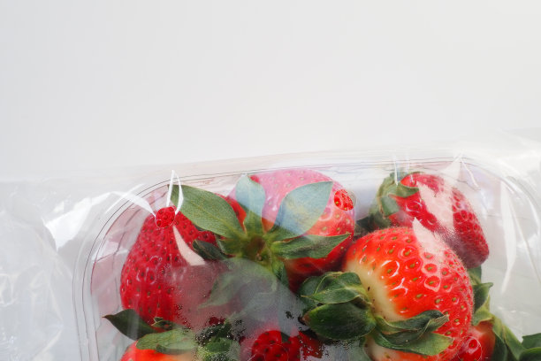 在白色背景上用塑料包装的成熟草莓。盛在容器里的新鲜美味浆果出售给顾客。保持食物新鲜。健康食品，维生素和微量元素图片下载