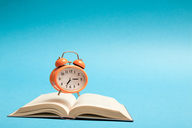 Flyind橙色复古风格闹钟和一本蓝色背景的书。自我发展和教育理念。图片下载