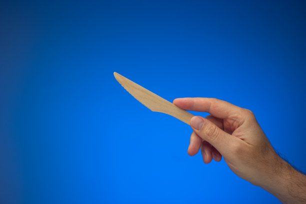 白人男性手持一次性、一次性、可生物降解的木刀。关闭工作室拍摄，孤立在蓝色背景图片下载