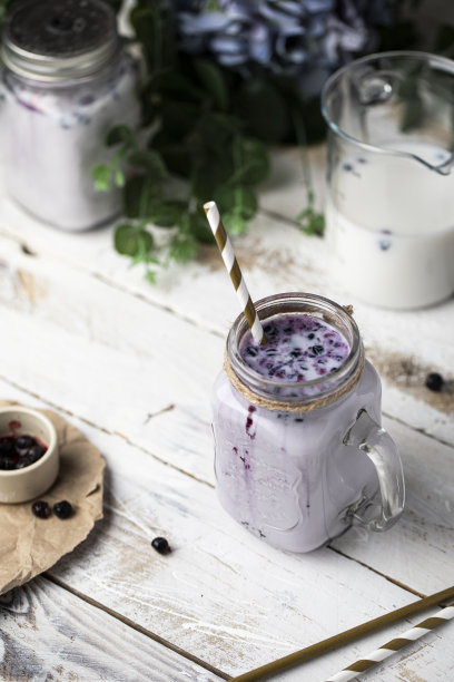 牛奶黑加仑冰沙在玻璃罐中与素食植物为基础的牛奶装饰花在桌子上。图片下载