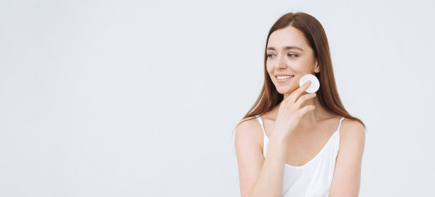 美丽的肖像快乐微笑的年轻女子与黑色长发和清洁新鲜的皮肤脸与棉垫在白色的背景，横幅图片下载