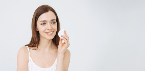 美丽的肖像微笑的年轻女子与黑色长发和清洁新鲜的皮肤脸与棉垫在白色的背景，横幅图片下载