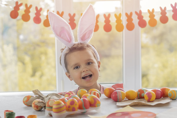 可爱的女孩头上戴着兔子耳朵，坐在窗边，看着复活节的装饰品图片下载