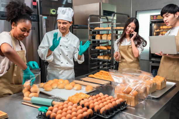亚洲男性和非洲女性穿着围裙的厨师，通过移动应用技术直播的小企业博主，面包店销售在线推广，新鲜面包。图片下载