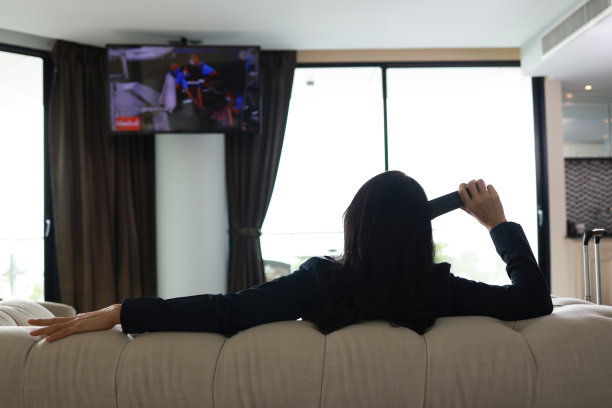 商务女性拿着遥控器看电视，下班后在酒店房间休息和放松，商务旅行的生活方式图片下载