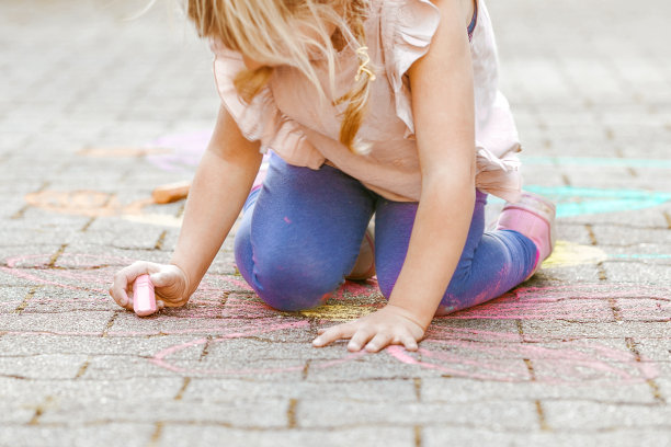 幼儿园的小女孩用彩色粉笔在后院的地上画花。积极快乐的蹒跚学步的孩子在沥青上画画和创造图片。夏季创造性的户外儿童活动。图片下载