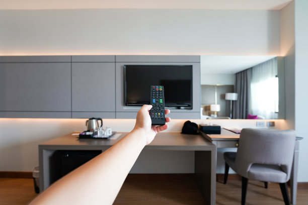 在泰国那空Phanom省的度假酒店房间里，一名男子手里拿着灰尘遥控器看电视，模糊了背景。图片下载