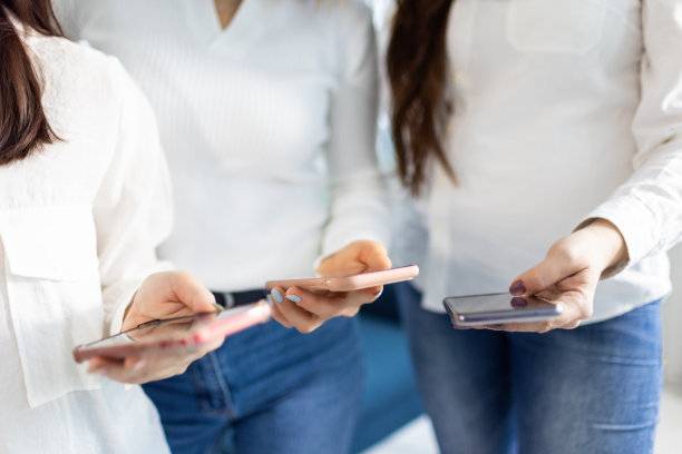 工作室里穿着衬衫和牛仔裤的女孩手里拿着三部智能手机图片下载