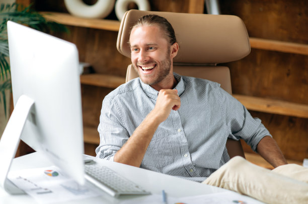 快乐自信有魅力的年轻成年经理或商人，坐在办公室里，腿放在桌子上，使用电脑，通过视频与同事或朋友交流，微笑友好图片下载