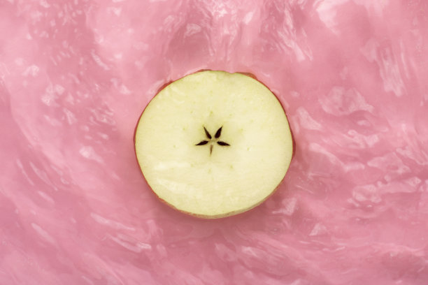 一片苹果在粉红色的水面上溅起水花。图片下载
