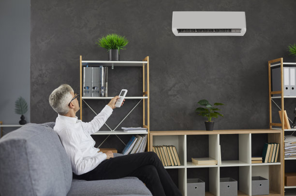 坐在办公室沙发上的男人用遥控器切换现代空调图片下载