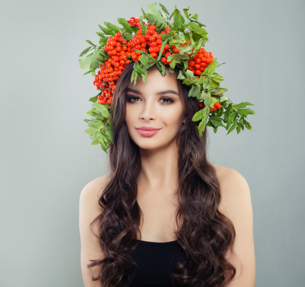 漂亮微笑的黑发女人与绿色的叶子和红色的浆果工作室肖像图片下载