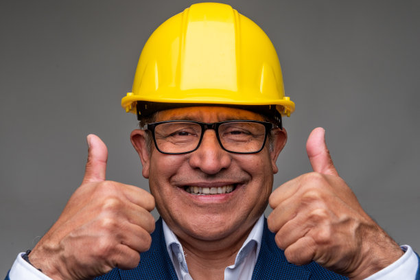 微笑的西班牙裔年长男子戴着一个艰苦的工作头盔前面部照片摆姿势，他的大拇指向上图片下载