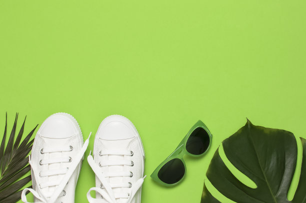 白色女性时尚运动鞋，时髦的太阳镜，绿色背景上的热带树叶。平面俯视图拷贝空间。女性的鞋子,配饰。时尚的白色运动鞋。夏天创意概念图片下载