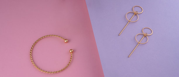 全景拍摄螺旋形手链和金色耳环对紫色和粉红色的背景与复制空间图片下载