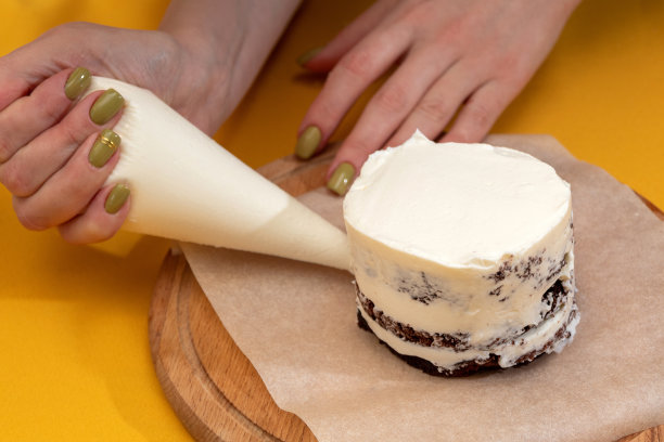 妇女手里拿着糕点袋，过程中把奶油摊在便当蛋糕上。关于甜点，食物的网站图片。有选择性的重点。图片下载