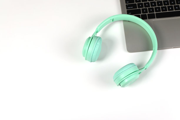 绿色耳机与笔记本电脑在白色表面。为音乐节、广播电台、音乐爱好者提供创意，与音乐一起生活，简约风格与现代。图片下载