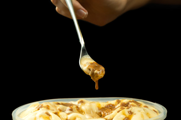 微距照片的甜点勺子与焦糖冰淇淋在一个冰淇淋容器前面的黑色背景与复制空间。图片下载