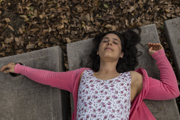 乐观的拉丁美洲女性(33岁)对春天的到来感到非常高兴。她仰面躺着，背景是干树叶。她穿着一件粉红色的花连衣裙。春天的概念。图片下载