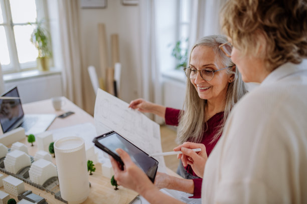 带着蓝图的成熟女性生态建筑师一起在办公室的平板电脑上工作。图片下载