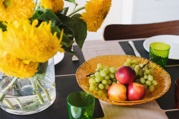 漂亮的盘子里有葡萄、桃子和一束向日葵在餐桌上。图片下载