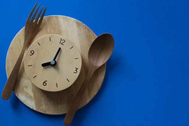 食物时钟勺子和叉子，健康的食物早餐概念在蓝色的桌子背景图片下载