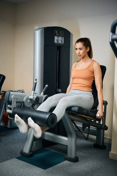 年轻的女运动员在健身俱乐部的腿部伸展机上锻炼。图片下载