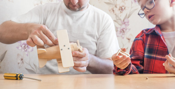 父亲节快乐，童年理念。父亲和儿子戴着眼镜，使用手工工具，用螺丝刀在家里的桌子上组装一个木制的构造器。图片下载