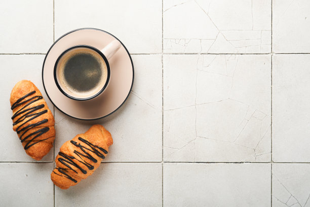 咖啡和羊角面包。有裂纹的旧瓷砖桌上放着浓缩咖啡和巧克力羊角面包。完美的羊角面包早餐。乡村风格。前视图。模拟。图片下载