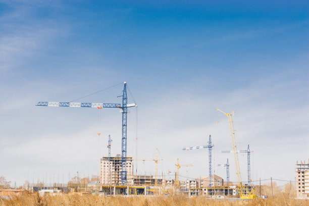 多层建筑的建造。塔吊在草原上建造高楼大厦图片下载