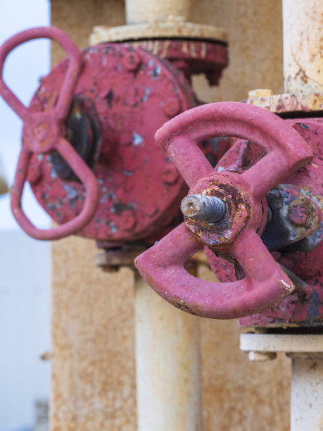 两个工业阀门用于燃气管道。一个又大又旧又生锈的煤气水龙头，红色油漆已经剥落。关闭一个大阀门丝锥轮图片下载