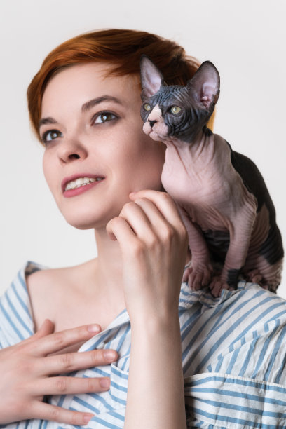 斯芬克斯小猫坐在快乐的红发年轻女子的肩膀上。选择性聚焦猫图片下载