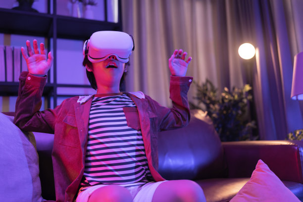 亚洲男孩戴着VR或虚拟现实眼镜，头戴式耳机站在客厅的电视机前玩视频游戏，在隔离期间的技术和创新概念霓虹灯夜生活方式图片下载