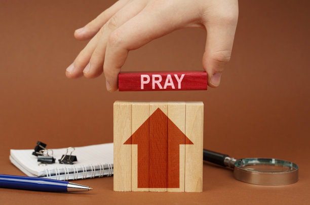 在棕色的表面是办公用品，木块，在手中是一个红色的块铭文-祈祷图片下载