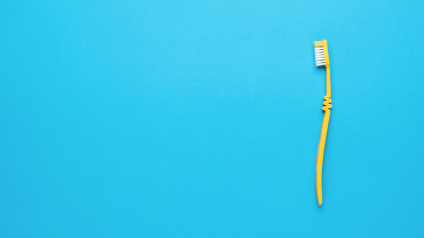 黄色牙刷，白色刷毛，蓝色背景。平的。图片下载
