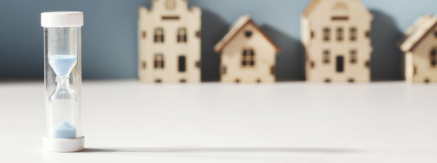 住房抵押、房地产市场、房地产需求概念。蓝色背景上的沙漏和小玩具屋。横幅选择聚焦图片下载