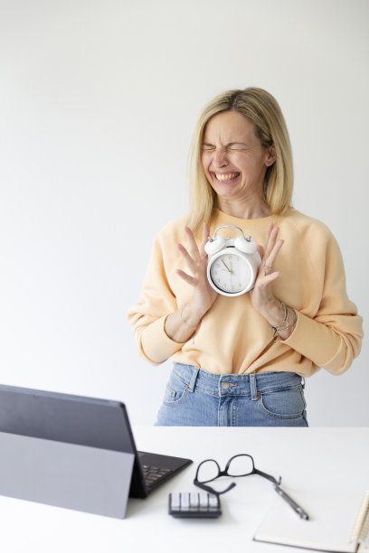 漂亮的金发女人站在吧台旁边手里拿着白色闹钟，时间是5点到12点图片下载