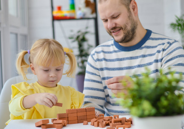 一个小女孩和一个年轻的白人父亲在玩粘土积木。幸福的家庭。通过游戏活动教育孩子。儿童教育游戏。图片下载