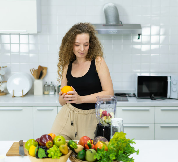 聪明的素食女性微笑着，快乐着，在厨房里用拷贝空间混合橘子、苹果、水果、蔬菜煮果汁。美丽的白人妇女烹饪健康的饮食水果或蔬菜在厨房图片下载