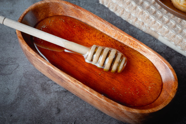 蜂蜜放在木碗里，灰色背景上有蜂蜜勺图片下载