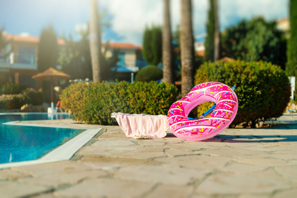 游泳池旁边的甜甜圈形状的橡胶圈。暑假的概念。图片下载