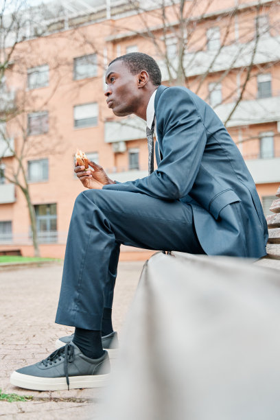 年轻的非裔美国办公室职员在户外吃午餐，坐在办公大楼附近的长凳上吃三明治，图片下载