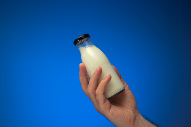 白人男性手里拿着带帽的小玻璃牛奶瓶。关闭工作室拍摄，孤立在蓝色背景图片下载
