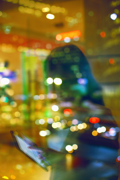 夜晚透过窗户玻璃，女人眼睛里的光反射在市中心触摸平板电脑设备图片下载