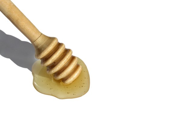 白色背景上洒了蜂蜜的木制勺。图片下载