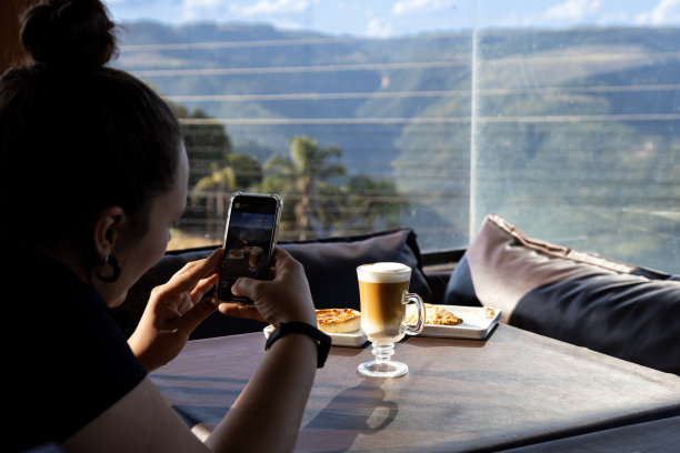 年轻女子在拍卡布奇诺和乳蛋饼早餐的照片。阳光透过玻璃窗图片下载