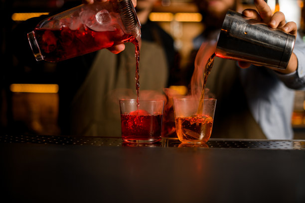 两个加冰的透明玻璃杯，调酒师小心翼翼地倒入各种明亮的热气腾腾的鸡尾酒图片下载