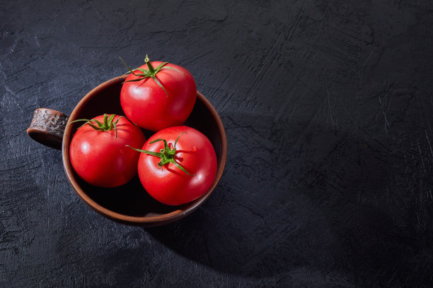 红色成熟的西红柿放在一个深色背景的碗里。获取新鲜的西红柿。图片下载