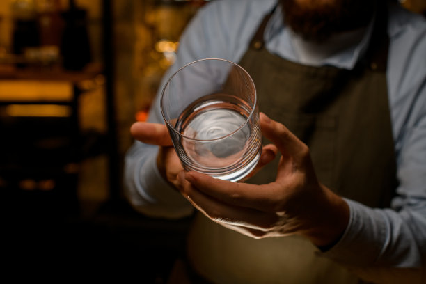男酒保的手正拿着一个透明的空酒杯斟酒图片下载